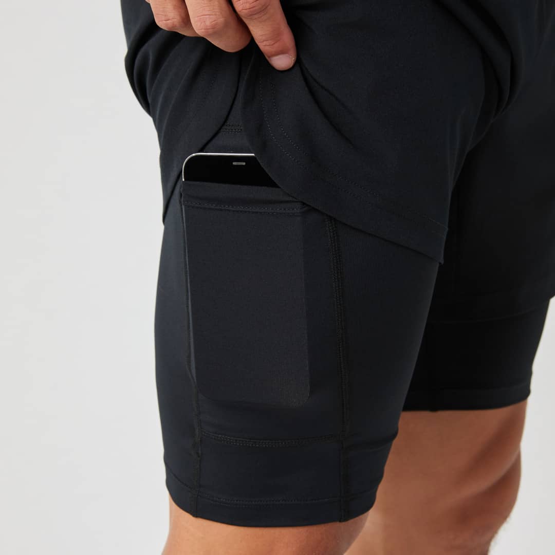 Close-up of a person wearing black athletic shorts with a phone partially visible in a side pocket, hand holding the fabric.
