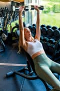 Woman doing incline dumbbell press at the gym, wearing white sports bra and green gym leggings from Björn Borg
