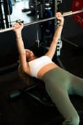 Woman doing a barbell bench press, wearing white sports bra and green tights from Björn Borg