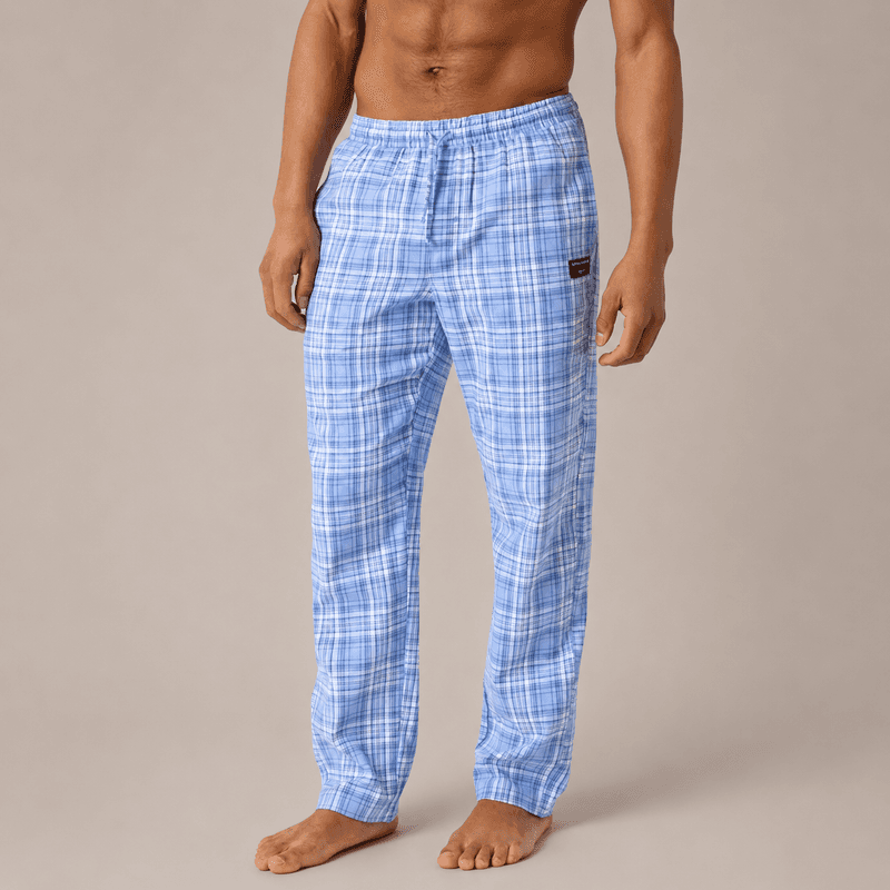 Man wearing blue plaid pajama pants, standing barefoot against a neutral background, upper torso not visible.