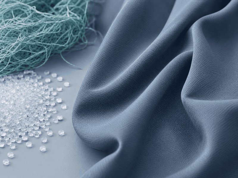 Blue fabric draped alongside white spherical beads and tangled light blue fibers on a smooth surface.