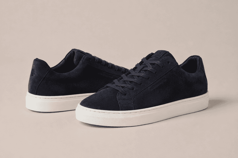 Pair of navy suede low-top sneakers with white rubber soles on a neutral background.