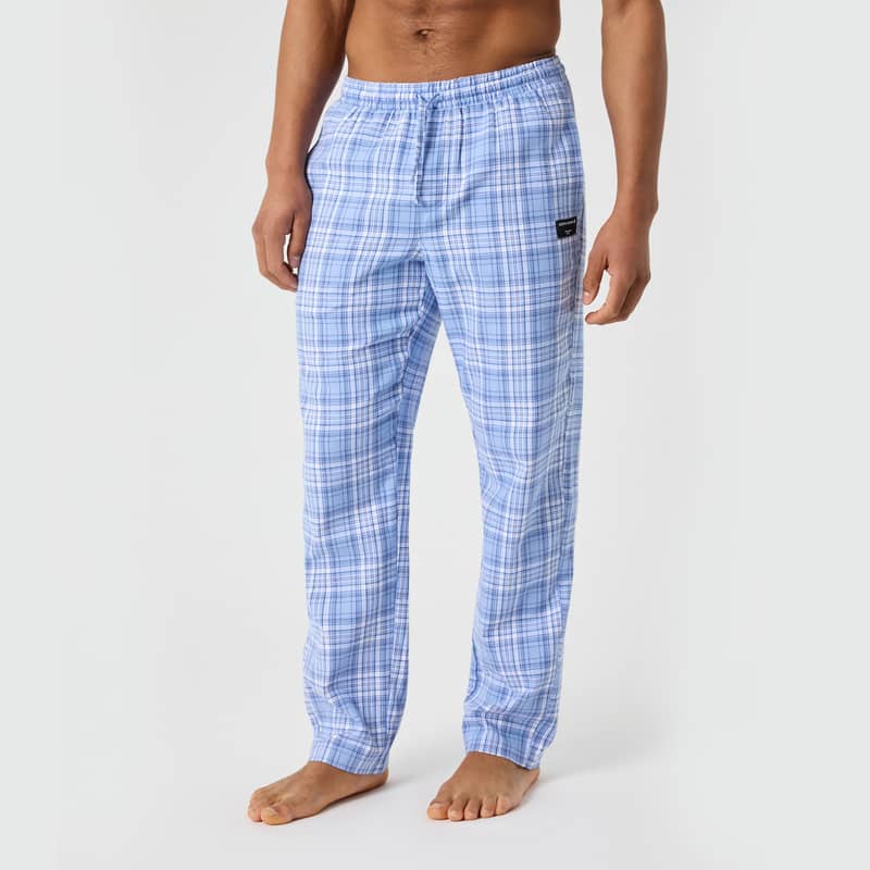 Man wearing light blue plaid pajama pants, standing barefoot against a plain background.