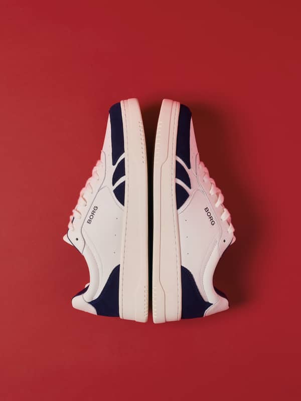 White and navy court sneakers displayed against a red background.