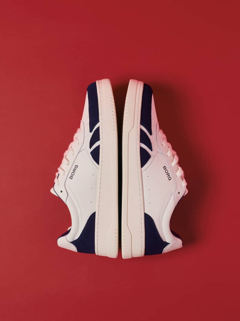 White and navy court sneakers displayed against a red background.
