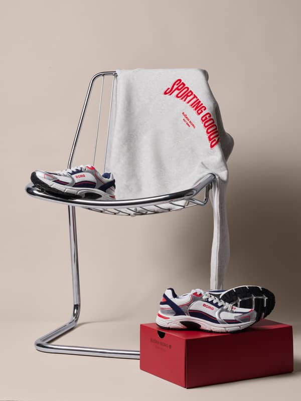A gray "Sporting Goods" sweatshirt on a chrome chair, with sneakers on a red box underneath.