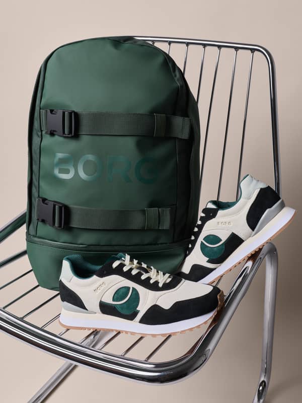 Green backpack displayed with retro running sneakers on a chrome chair.