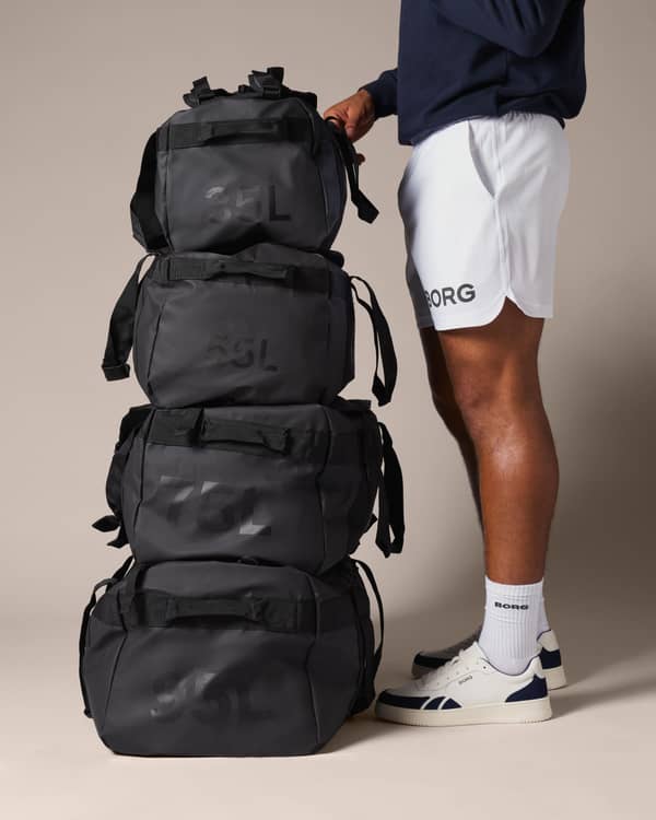 Person in sportswear standing next to a stack of four black duffel bags marked 35L, photographed against a neutral background.