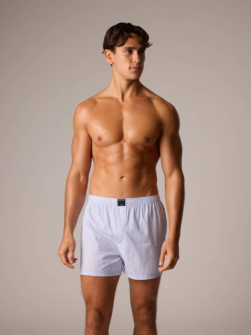 A shirtless man wearing striped boxer shorts stands confidently against a neutral background.