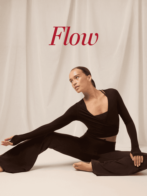 A woman in a dark outfit poses gracefully on a light beige floor with "Flow" written above her, against a soft fabric backdrop.
