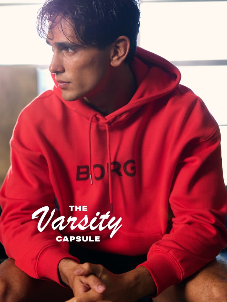 Man in a red hoodie with "BORG" text, sitting indoors, looking to the side. Text on image reads "The Varsity Capsule."
