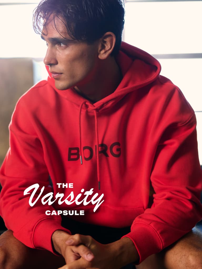 A person wearing a red hoodie with "BORG" written on it, sitting in a relaxed posture. The text "The Varsity Capsule" is displayed.