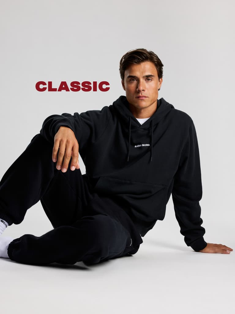A person in a black hoodie and sweatpants sits against a plain background, with the word "CLASSIC" in bold red text beside them.