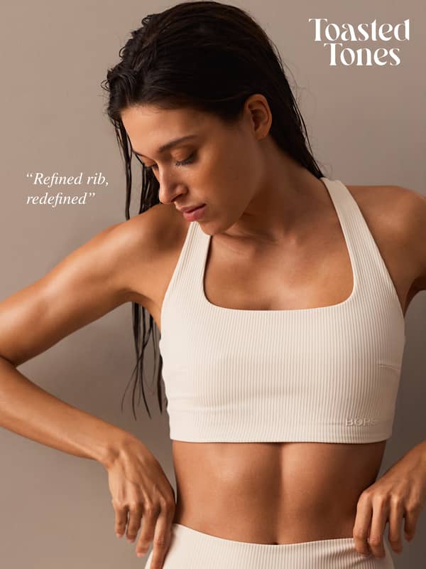 A woman in a beige ribbed sports bra and leggings poses against a neutral background with "Toasted Tones" and text "Refined rib, redefined" on display.