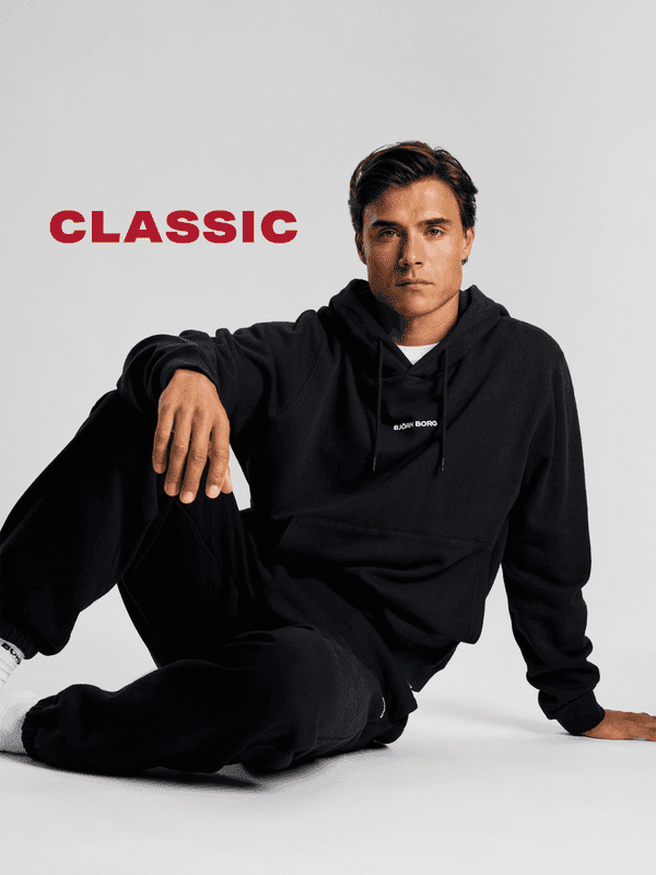 A person in a black hoodie and sweatpants sits on the floor against a plain backdrop. The word "CLASSIC" is written in bold red letters.