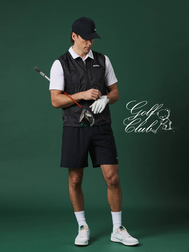 Man in a golf outfit holding a club, wearing a cap, vest, and shorts, stands against a green background with "Golf Club" logo.