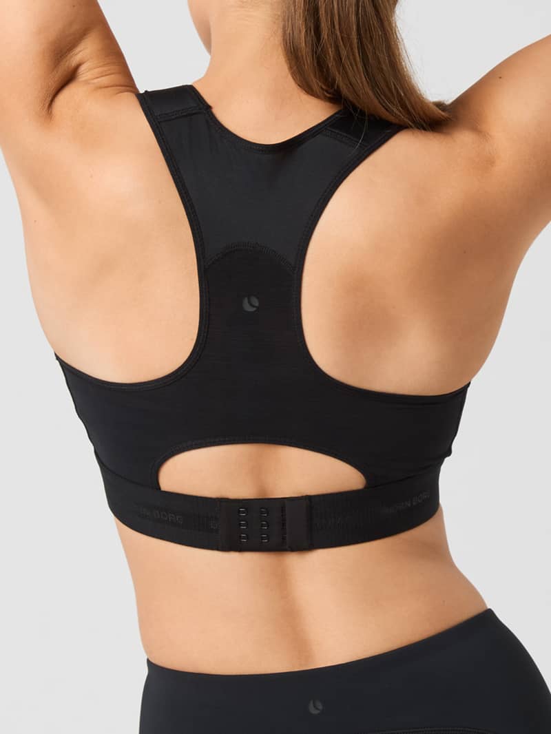 The back view of a person wearing a black sports bra with a racerback design and adjustable strap closure, arms raised.