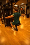 A man dowing back flyes exercise on the machine at the gym. He is wearing a blue-green set with Björn Borg t-shirt and shorts plus white Björn Borg shoes.