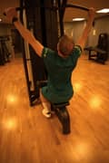 Man in Borg T-shirt and shorts doing a lat pul down on the machine at the gym