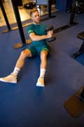 Man doing russian twists with a dumbbell. He is wearing a green Borg t-shirt and matching shorts, together with white socks and sneakers from Björn Borg