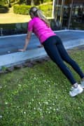 A blond woman outdoors in a pink Borg T-shirt, black Borg Running Tights and white Björn Borg sneakers, doing a bench push up