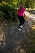 A blond woman outdoors in a pink Borg T-shirt, black Borg Running Tights and white Björn Borg sneakers, running in place