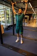 Man doing a push press with dumbbells. He is wearing a green Borg t-shirt, matching shorts and white sneakers from Björn Borg