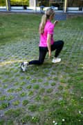 A blond woman outdoors in a pink Borg T-shirt, black Borg Running Tights and white Björn Borg sneakers, doing lunges