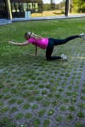 A blond woman outdoors in a pink Borg T-shirt, black Borg Running Tights and white Björn Borg sneakers, doing bird dog exercise