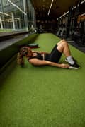 Woman doing heel touches at the gym. She is wearing a black sports bra, black bike shorts and black sneakers from Björn Borg.