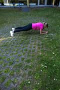 A blond woman outdoors in a pink Borg T-shirt, black Borg Running Tights and white Björn Borg sneakers, doing an elbow plank