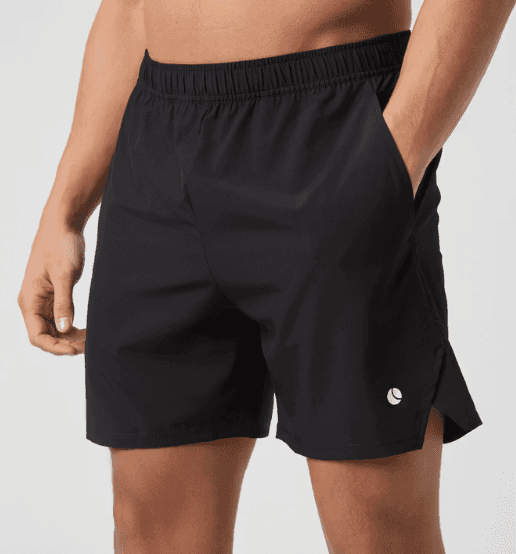Man wearing black athletic shorts with an elastic waistband, standing with one hand in pocket, on a light gray background.