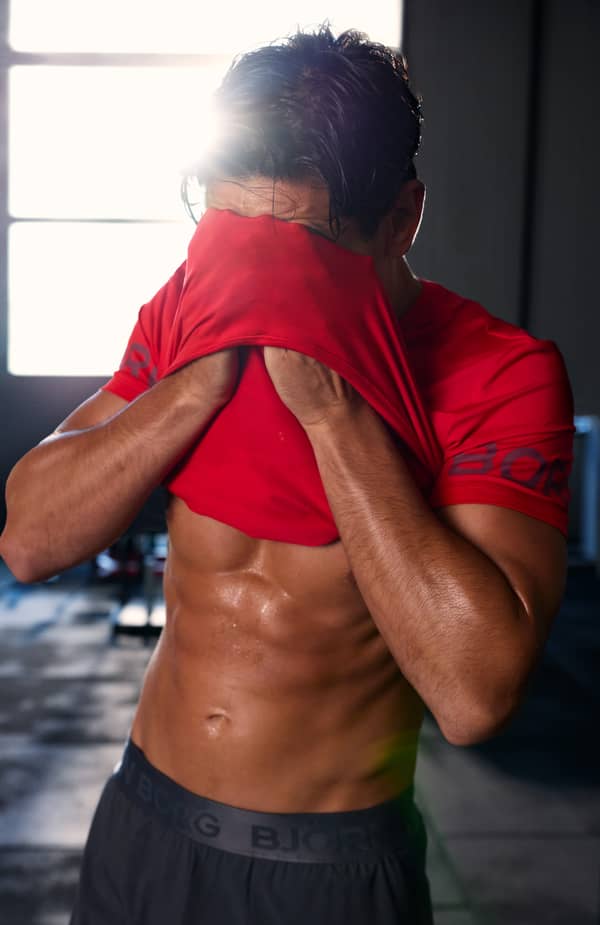 Man removing a red training T-shirt after a workout in a gym.