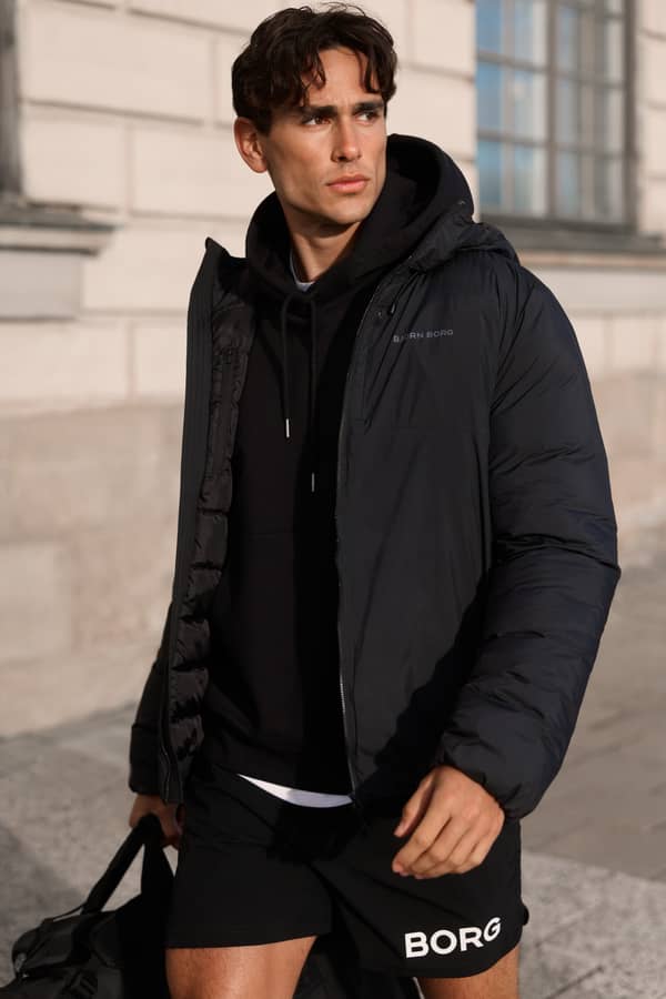 Man wearing a black jacket, black hoodie and training shorts outdoors