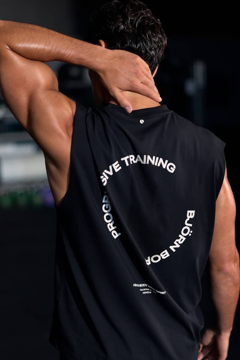 Back view of a man wearing a black sleeveless training top with a Progressive Training graphic print.