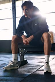 Man wearing a black hoodie seated on a gym bench