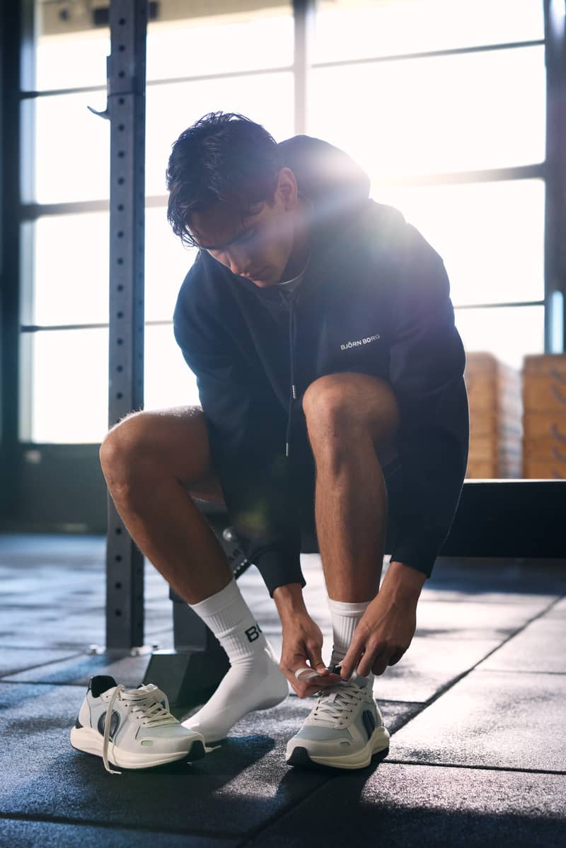 Man tying training shoes while wearing a black hoodie in a gym