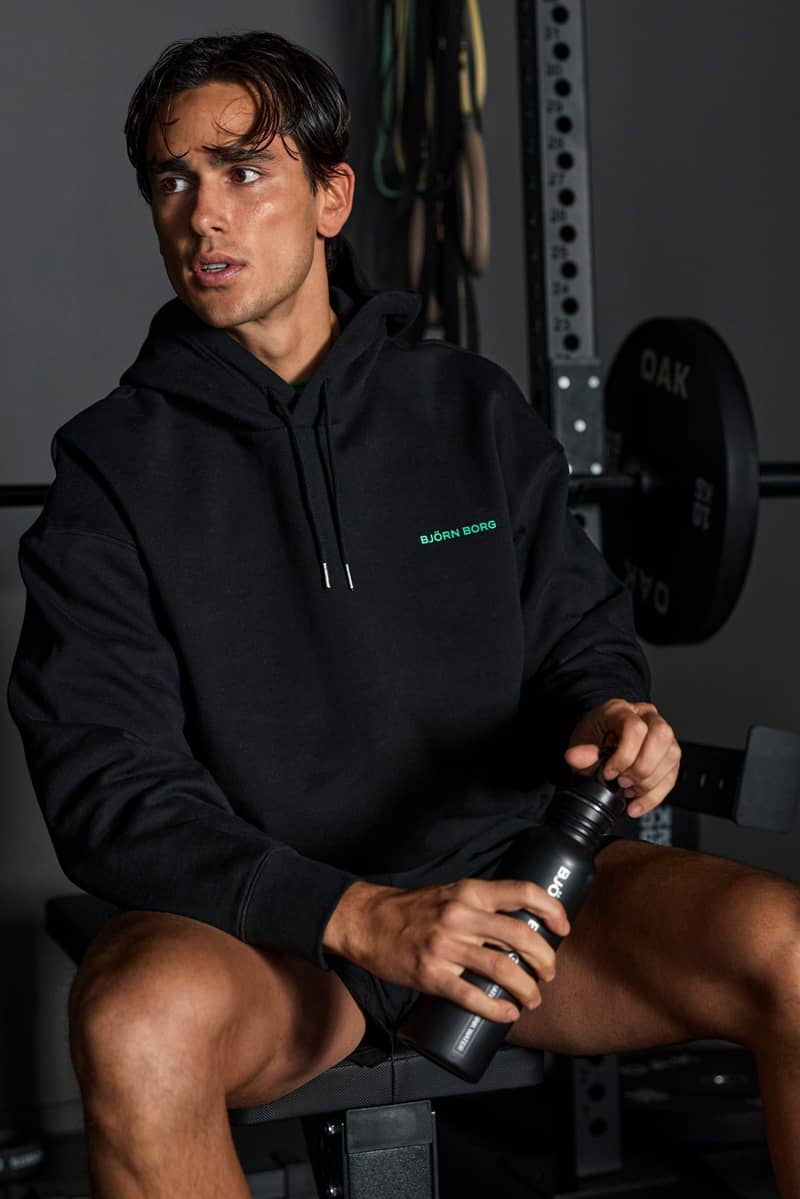 Man sitting on a gym bench in a black Björn Borg hoodie and shorts.