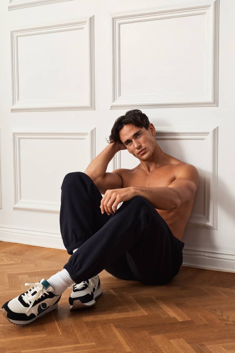 Man sitting on the floor wearing black joggers and retro running sneakers.