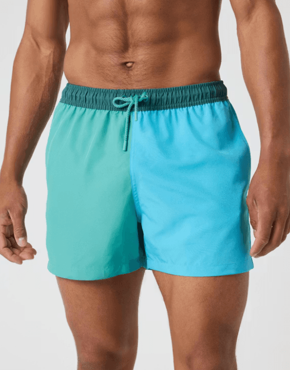 Man wearing two-tone green and blue swim trunks with a dark waistband and drawstring, standing against a light background.