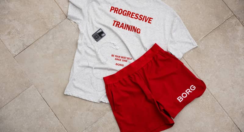 Gray T-shirt with "Progressive Training," red shorts with "BORG," an MP3 player, and earphones on a tiled floor.