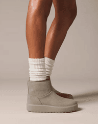 Woman wearing beige ankle boots and white ribbed socks, standing on a neutral background.