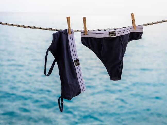 Two pieces of black and white swimwear hang on a clothesline with wooden clothespins, against a backdrop of calm blue sea.