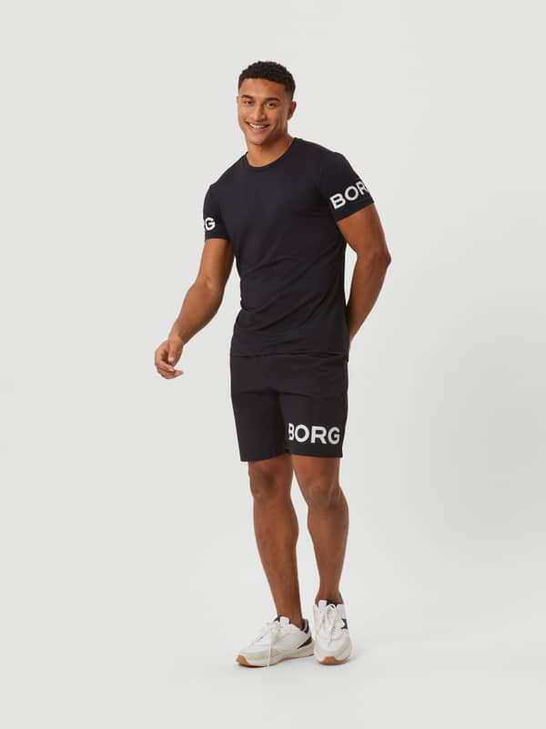 Full-body front view of a man wearing 9-inch Black Beauty (Black) Borg Shorts with a white logo for training.