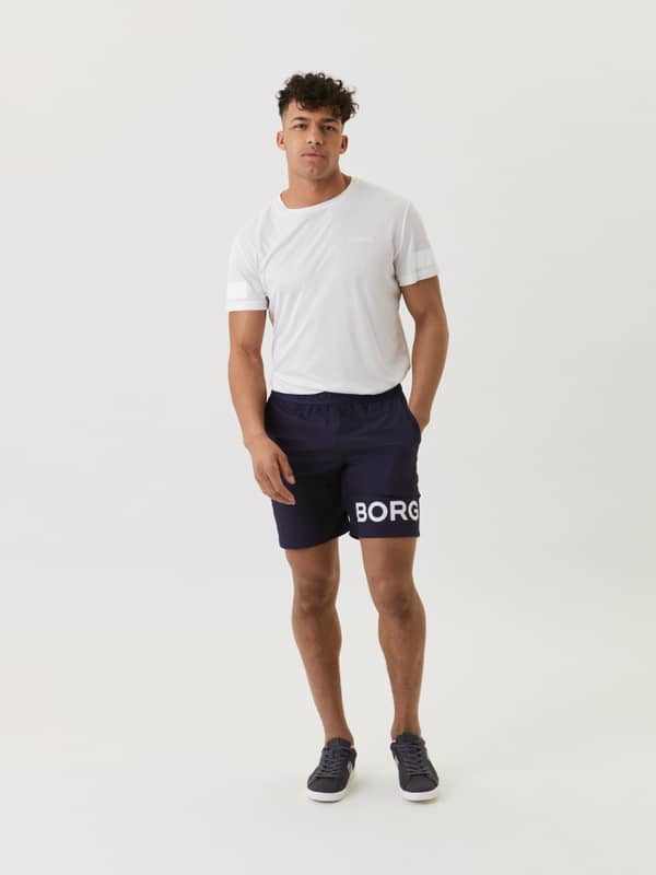 Full-body front view of a man wearing navy Borg Shorts with a white logo, designed for training style and performance.