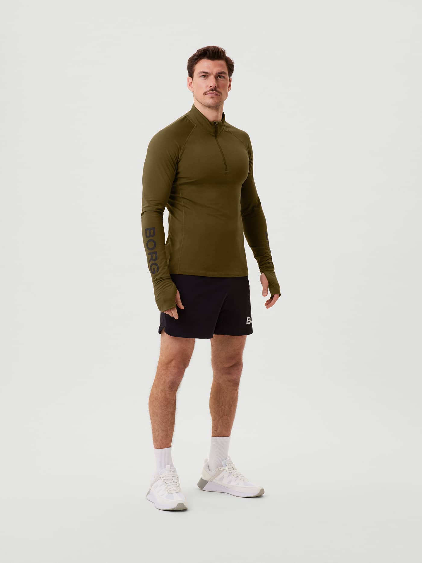 Vooraanzicht van een man in de Borg Midlayer Half Zip in Dark Olive (Groen) met duimgaten en zwart logo voor training. - Image 2