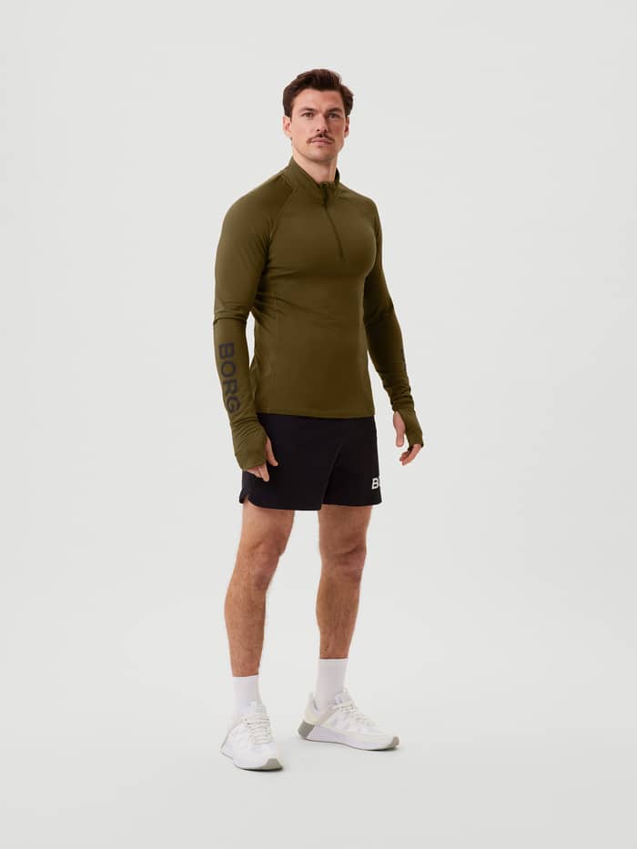 Vooraanzicht van een man in de Borg Midlayer Half Zip in Dark Olive (Groen) met duimgaten en zwart logo voor training. - Image 2