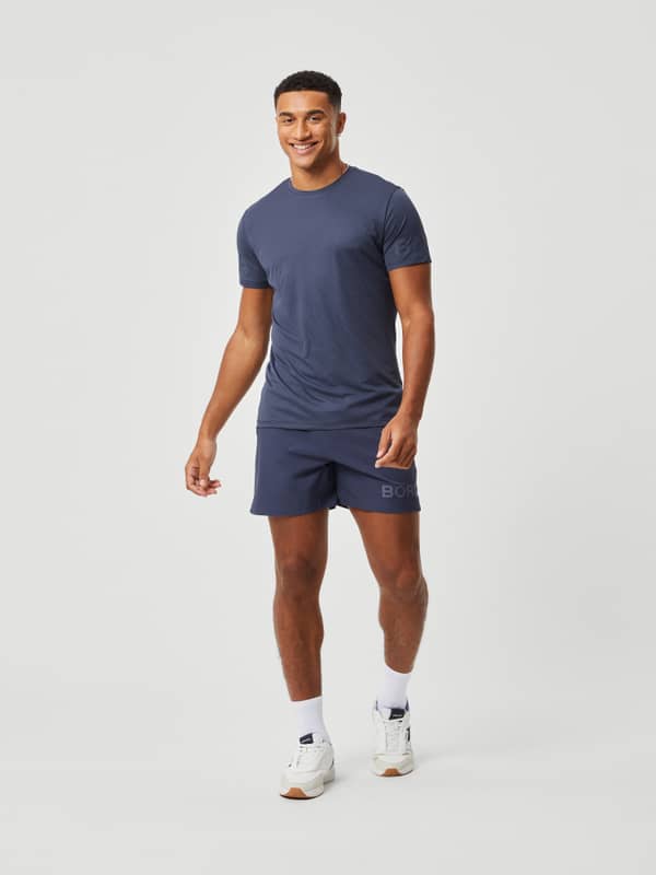 Full-body front view of a man wearing technical Borg Short Shorts in Odyssey Gray (Blue) for stylish training performance.