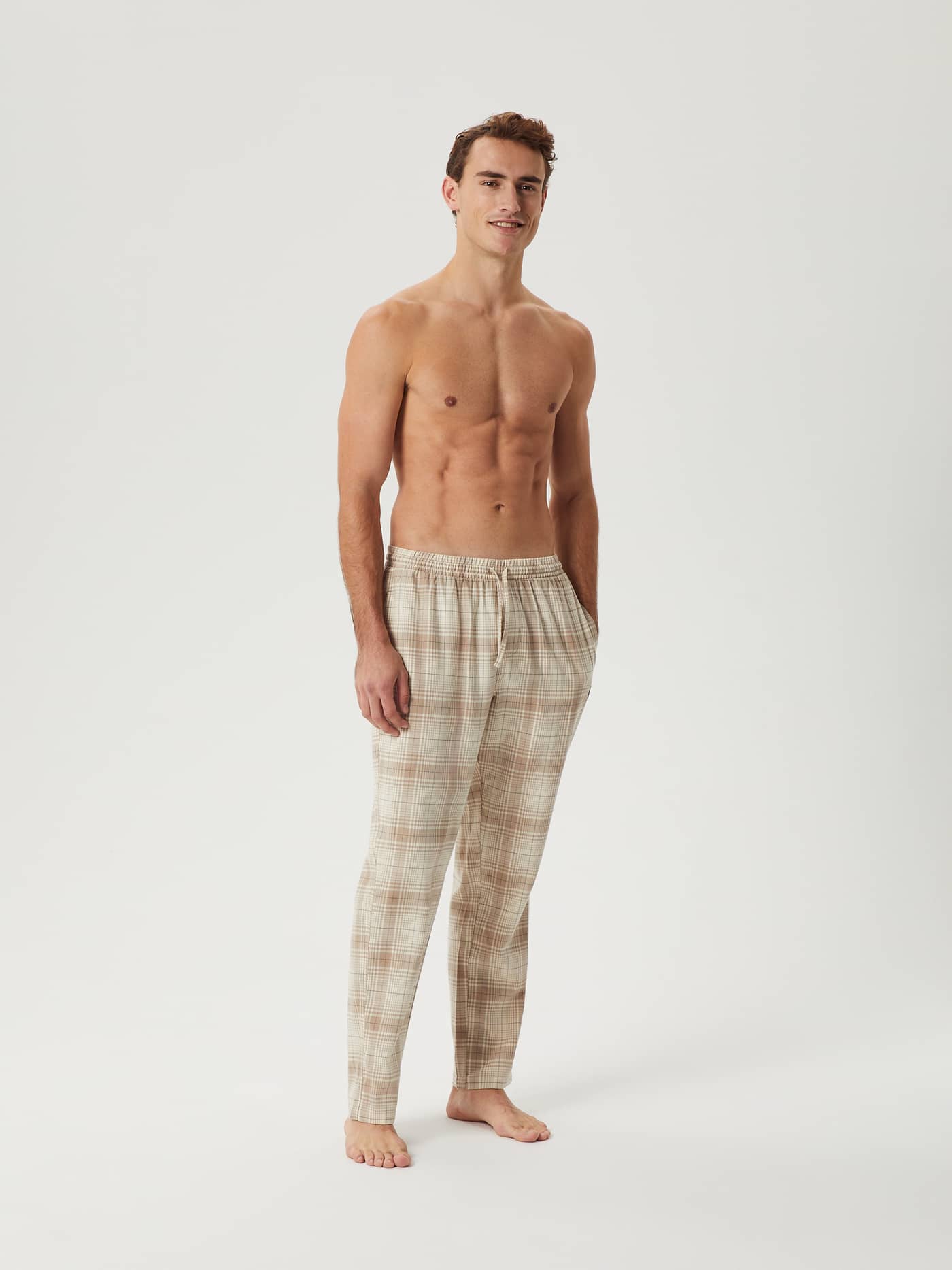 Male model standing in a studio wearing the Björn Borg Core Flannel Pyjama Pants in a beige and brown plaid pattern. - Image 3