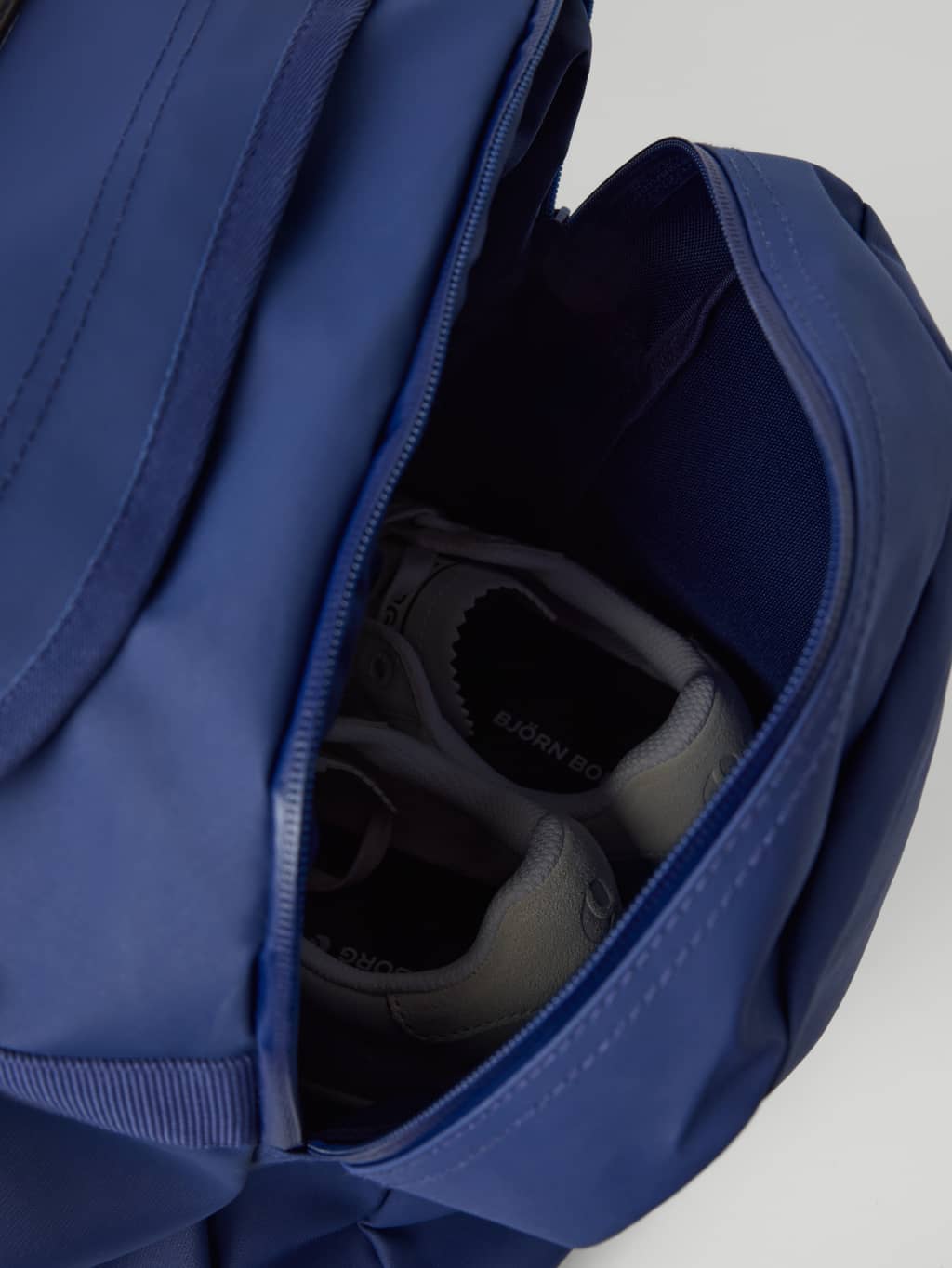 Water-resistant wet pocket on the Borg Duffle Bag 55L in Estate Blue (Blue) shown with athletic shoes stored inside. - Image 3